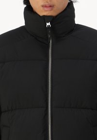 Must must-jakk, millel on kõrge krae, tikandiga disain ja hõbedane lukustus. Sujuv viimistlus ja minimalistlik stiil.