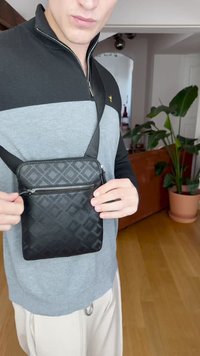 Borsa a tracolla nera con motivo in rilievo geometrico, chiusura con zip, design piatto e tracolla regolabile. Texture liscia, forma compatta.