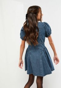 Džínové šaty s nafúknutými rukávmi, priliehavým živôtikom a rozšírenou sukňou. Tmavomodrá farba s jemnými švami a zapínaním na gombíky na chrbte.