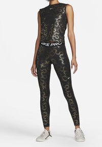Conjunto deportivo negro que incluye una camiseta sin mangas con patrones florales dorados y leggings a juego, acentuado por una banda negra marcada "NIKE PRO."