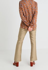 Bruine bloemen blouse met lange mouwen en blauwe patronen, gecombineerd met lichtbeige flared broek en rode blokhak sandalen van achteraan bekeken.