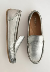 Metalne srebrne slip-on loaferice s ušivenim dizajnom, mekanim gornjim dijelom i teksturiranim potplatima. Unutrašnjost ima glatku smeđu završnu obradu s ventilacijskim otvorima.