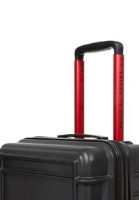 Black hard-shell suitcase with a textured finish, red telescopic handle labeled "BUILT TO RESIST," and a black rubber grip.