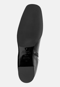 Semelle de chaussure en cuir noir avec une surface lisse, un bout arrondi et un nom de marque embossé distinct. Présente un détail de fermeture éclair sur le côté.