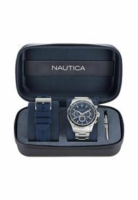 Orologio Nautica in una custodia blu con zip, comprende un orologio in tonalità argento con quadrante blu e cinturino in silicone blu. Inclusa una chiave per le regolazioni del cinturino.