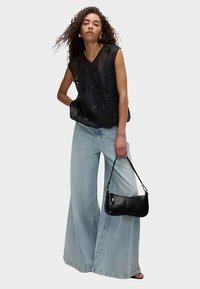 Czarny bezrękawnik z detalem w postaci kokardy na przodzie, zestawiony z jasnoniebieskimi szerokimi jeansami. Modelka trzyma małą czarną torebkę.