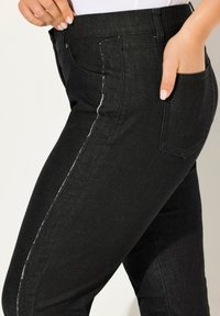 Jeans in denim nero con un design aderente e cuciture bianche a contrasto lungo le cuciture laterali; includono tasche posteriori.