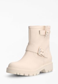 Botas de tobillo beige hechas de cuero texturizado, con dos correas de hebilla, herrajes plateados y una suela gruesa y texturizada.