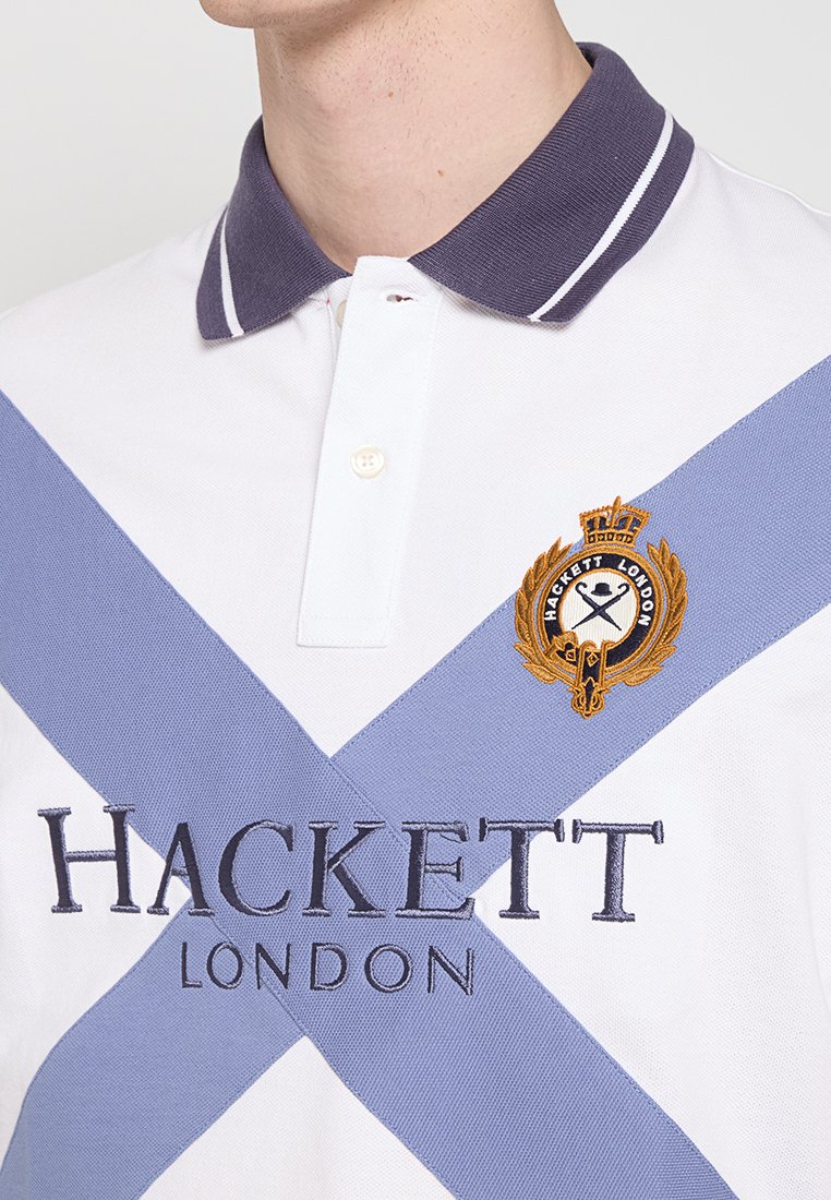 Polo-shirt blanc avec une rayure diagonale violet et bleu clair. Présente une broderie "HACKETT LONDON" et un emblème doré sur la poitrine.