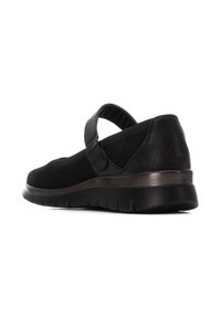 Zapatos de malla negra con una correa, punta redondeada y una suela de goma flexible con detalles texturizados en el talón y la parte inferior.