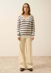 Sweter w paski w kolorze kremowym i granatowym, wykonany z miękkiego materiału. Zestawiony z jasno beżowymi spodniami z szerokimi nogawkami z sztruksu oraz brązowymi butami.