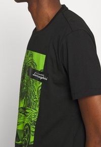 Černé tričko s krátkým rukávem s velkým zeleným grafickým designem auta a palmami, s černou nálepkou čtoucí "Lamborghini."