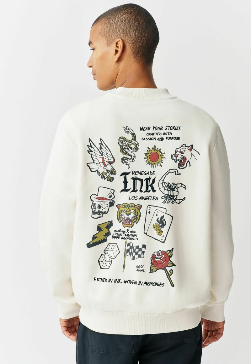 Crewneck Sweatshirt in Creme mit mehrfarbigen Tattoo-ähnlichen Grafiken, darunter ein Totenschädel, eine Schlange, ein Adler und Rosen, mit gerippten Bündchen.