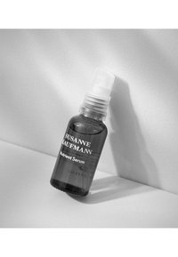 Czarna szklana butelka serum z przezroczystą pompką. Etykieta z białym tekstem "Susanne Kaufman Nutrient Serum". Gładka powierzchnia.