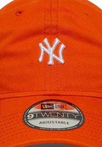 Casquette orange avec logo "NY" brodé en blanc, design réglable, forme structurée et tissu texturé. Étiquette indiquant le style 9TWENTY.