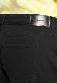 Zwarte spijkerbroeken van denim met een klassiek ontwerp, voorzien van een leren label op de tailleband en een achterzak. Glad textuur, minimale stiksels.