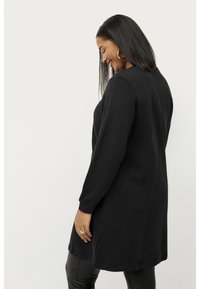 Tunique noire à manches longues avec une coupe décontractée, fabriquée en tissu doux. L'ourlet tombe au milieu des cuisses, avec des poignets côtelés et un col rond.