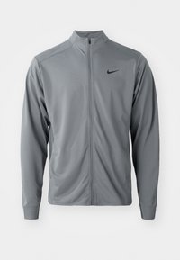 Grå lynlåsjakke lavet af glat, letvægtsstof. Har en ståkrave og et sort Nike-logo på den øverste venstre side.