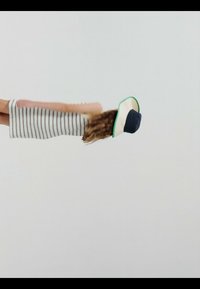 Kobieta w sukience w paski i kapeluszu z szerokim rondem pochyla się do przodu na jednolitym białym tle.