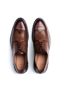 Chaussures oxford en cuir marron avec des détails brogue, présentant un bout arrondi, un système de laçage et une finition brillante. Semelle en caoutchouc noire.