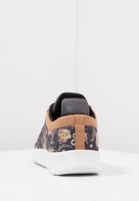 Baskets avec un motif floral sur tissu noir, accents en daim marron, et semelle en caoutchouc blanche. Dotées d'un rembourrage à l'arrière pour le confort.