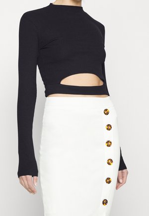 Schwarzes, geripptes Langarmoberteil mit Cut-Out-Design, kombiniert mit einem weißen Rock, der seitlich dekorative gelbe Knöpfe hat.