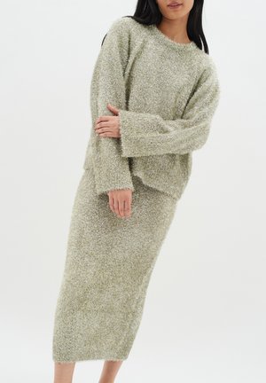 Stickad set i mjukt, texturerat, ljusgrönt material. Oversized tröja med sänkta axlar och en figurnära midi-kjol med råa fållar.