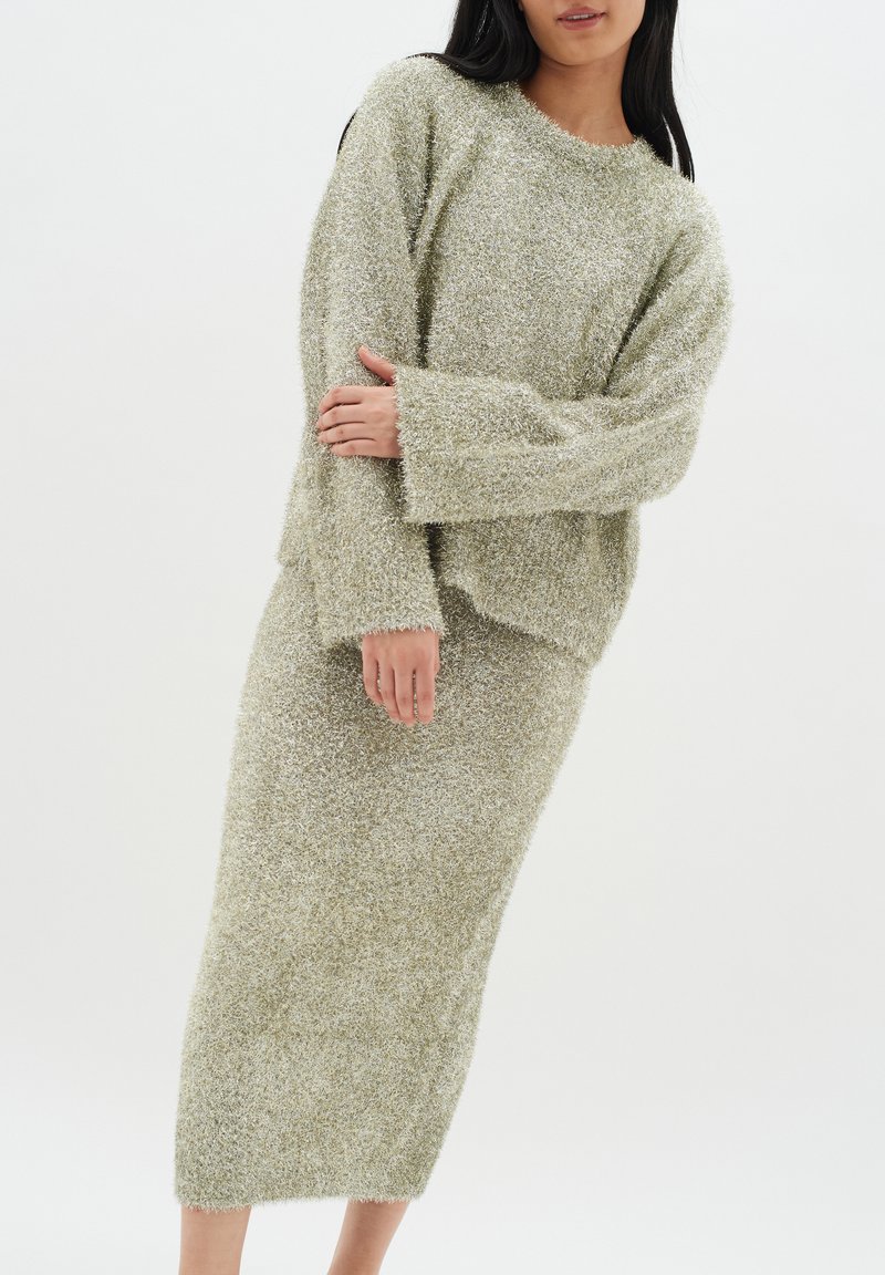 Stickad set i mjukt, texturerat, ljusgrönt material. Oversized tröja med sänkta axlar och en figurnära midi-kjol med råa fållar.