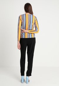 Randig långärmad topp i flera färger: gul, blå och svart; kombinerad med svarta byxor och ljusblå högklackade skor.