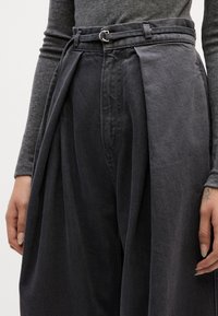 Pantalones oscuros de talle alto, con plisados y pierna ancha, que cuentan con un cinturón con herrajes de plata. Están elaborados en un tejido de denim texturizado.