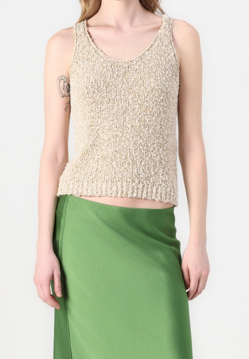 Top de tirantes de punto beige con escote redondeado y dobladillo acanalado, combinado con una falda de satén verde. La tela parece texturizada y suave.