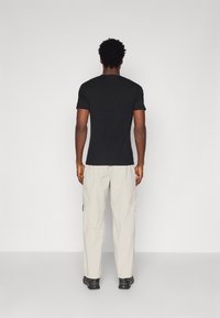 Black short-sleeve t-shirt paired with light beige cargo pants. The outfit features a relaxed fit and is complemented by black footwear.