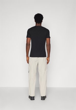 Black short-sleeve t-shirt paired with light beige cargo pants. The outfit features a relaxed fit and is complemented by black footwear.
