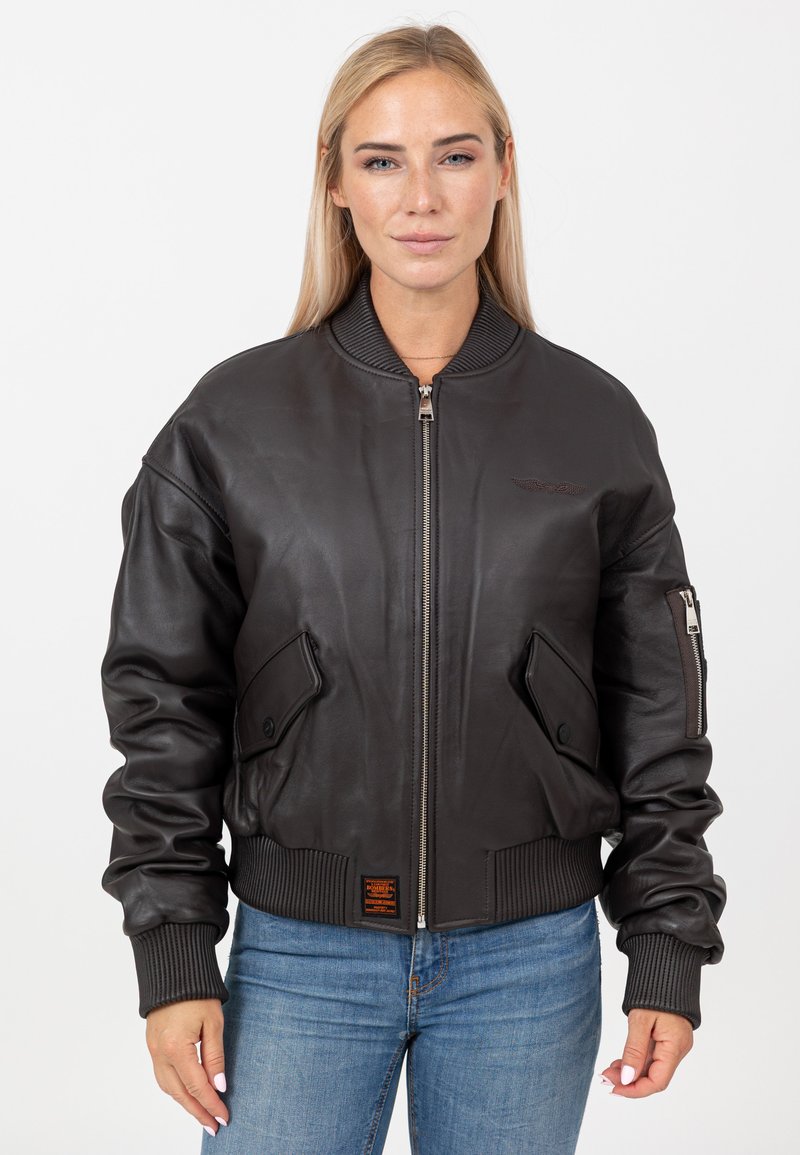 Brązowa skórzana kurtka bomberka z prążkowanym kołnierzem i mankietami, z zapięciem na zamek błyskawiczny, dwoma przednimi kieszeniami oraz małym emblematem na piersi.