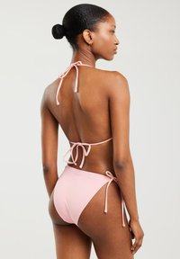 Różowy biustonosz w stylu halter z zaciskami, otwartym plecami i bezszwowym designem. Wykonany z gładkiego, elastycznego materiału dla zapewnienia komfortu i idealnego dopasowania.
