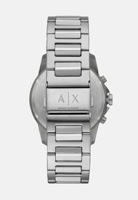 Roostevabast terasest kell, millel on ühendatud käevõru, poleeritud viimistluse, graveeritud logo ja ümmargune korpus minimalistliku disainiga.