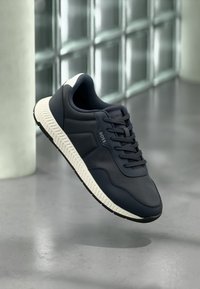 Baskets bleu marine en matériau synthétique avec une finition texturée, dotées d'une semelle blanche, d'une semelle extérieure en caoutchouc noir et de lacets.