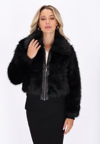 Zwarte faux fur jas met een ritssluiting aan de voorkant, voorzien van een kraag en ribbelmanchetten. De jas heeft een cropped ontwerp en een zachte, gestructureerde oppervlakte.