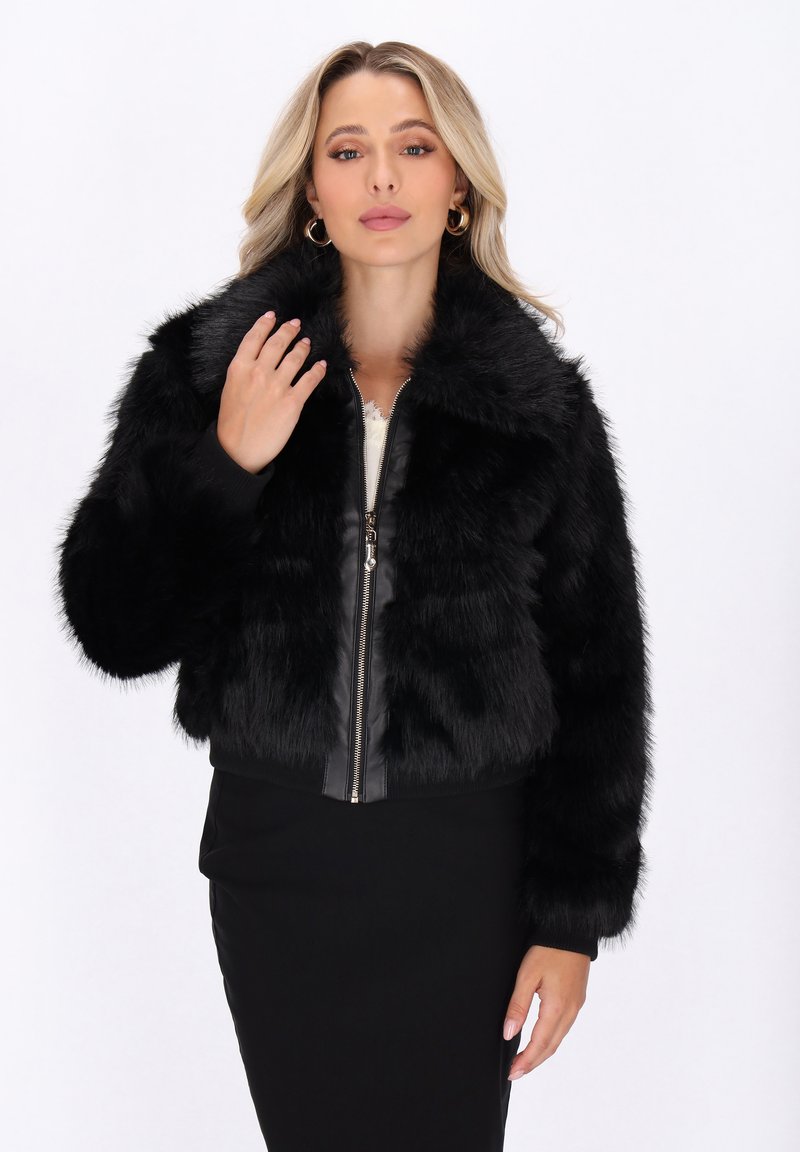 Zwarte faux fur jas met een ritssluiting aan de voorkant, voorzien van een kraag en ribbelmanchetten. De jas heeft een cropped ontwerp en een zachte, gestructureerde oppervlakte.