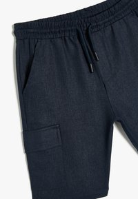 Mørkeblå shorts lavet af blødt stof, med elastisk talje med snoretræk, sidelommer og en cargo-lomme på benet.