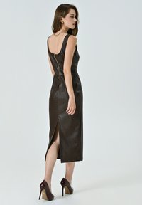 Braunes Kunstlederkleid mit Krokodilmuster, ärmelloses Design, Reißverschluss hinten und Schlitze an der Seite. Getragen mit bordeauxfarbenen High Heels.