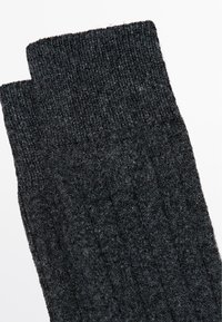 Gebreide zwarte sokken met een geribbelde textuur, voorzien van een hoge boord. Gemaakt van een zacht, warm materiaal, geschikt voor casual gebruik.