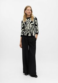 Pull noir et crème à rayures zébrées avec un col ajusté, associé à un pantalon noir large avec des plis avant et une coupe décontractée.