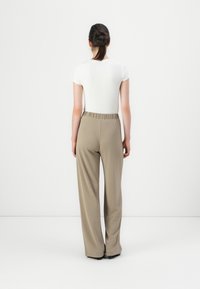 White fitted short-sleeve top paired with loose beige pants featuring an elastic waistband, textured fabric, and straight-leg design.