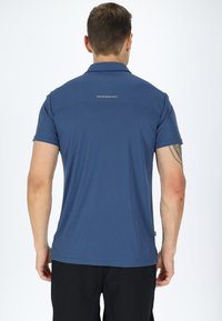 Blå polo skjorte med kortærmer, der har et tekstureret mønster og et diskret logo på ryggen. Materialet virker åndbart og komfortabelt.