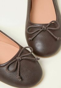 Braune Leder-Ballettschuhe mit strukturierten Oberflächen, runder Spitze und dekorativer Schleifenverzierung. Das Innere ist hellbeige.