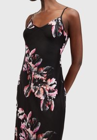 Svart blommig klänning med tunna axelband, som har livfulla rosa och vita blommönster. Slät tyg med en figurnära passform.