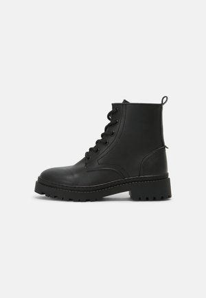 Botas de tobillo de piel negra con punta redonda, parte delantera con cordones y suela de goma texturizada. Cuenta con una pestaña y detalles de costura.