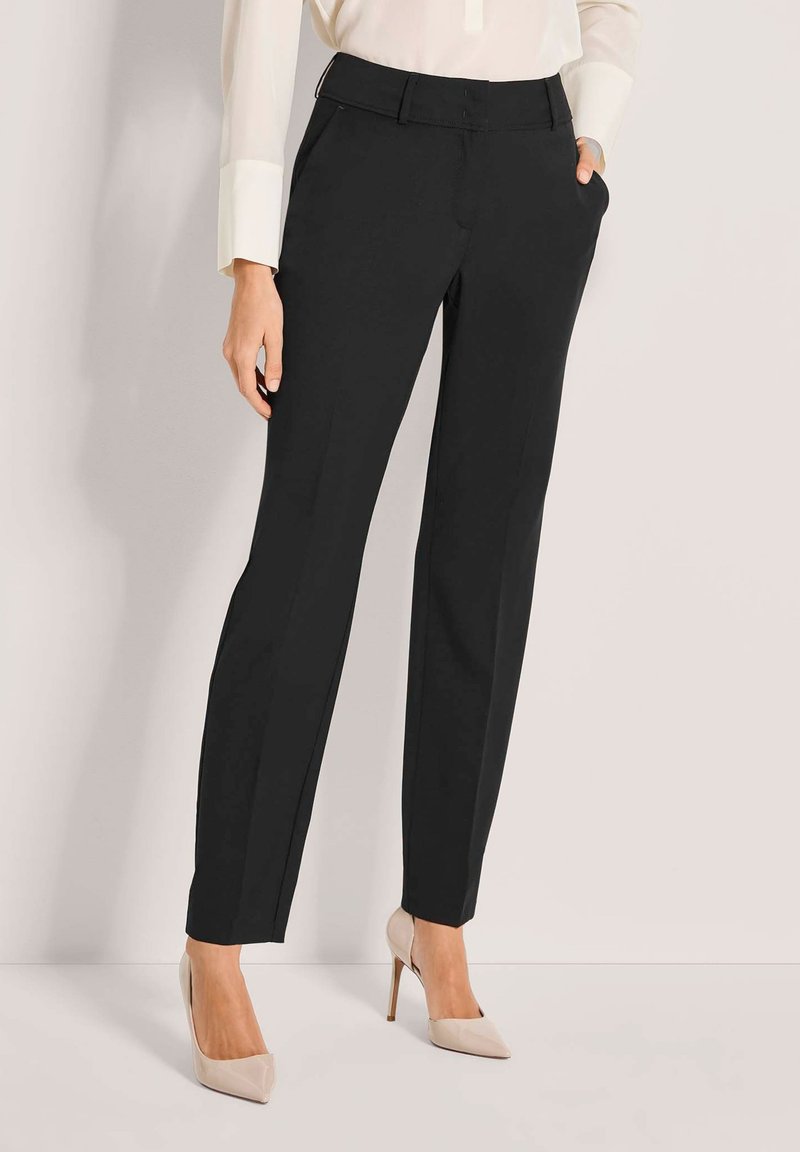 Schwarze maßgeschneiderte Hosen mit geradem Bein, ausgestattet mit Fronttaschen und einer glatten Textur. Kombiniert mit nudefarbenen High Heels.