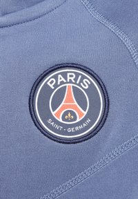 Un tissu bleu avec une texture lisse présente un patch brodé rond. Le patch affiche "PARIS" et la Tour Eiffel en rouge, avec "SAINT-GERMAIN" en dessous.